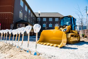The construction zone at the Ronald McDonald House. The ground is dirt. Shovels and hard hats are displayed in front of a digger.