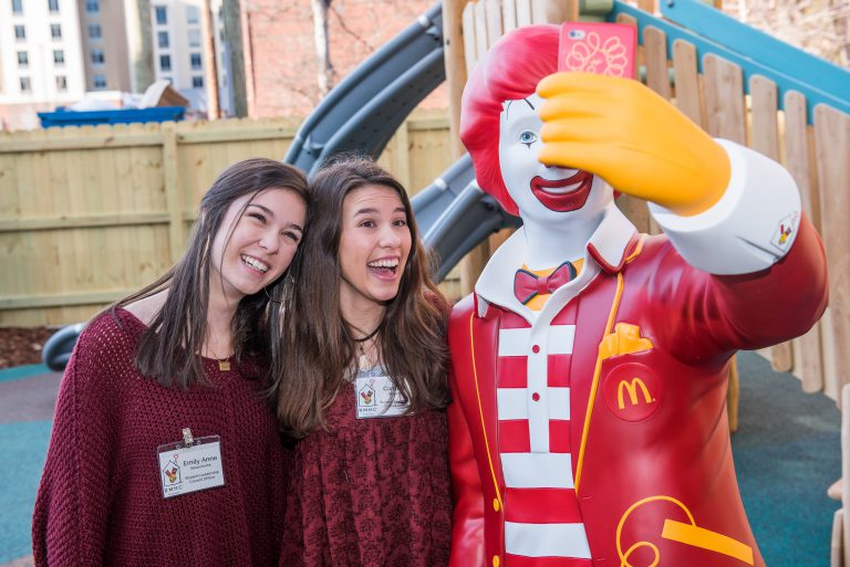 Two Student Leadership Council members pose for a picture with the Ronald statue on the playground.