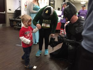 A young boy, who just had his face painted, says hello to Batman.