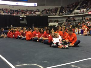 RMHCA kids sit on the elevated stage with Auburn gymnasts.
