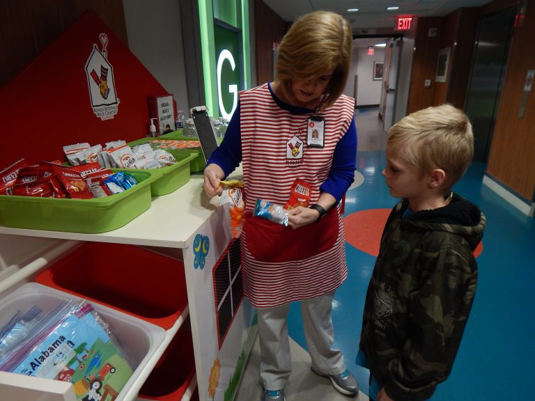 Volunteer Lisa Bolton tells a child about the available snacks on the Happy Wheels Cart.