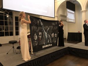 Two women hold up a one-of-a-kind KISS painting.