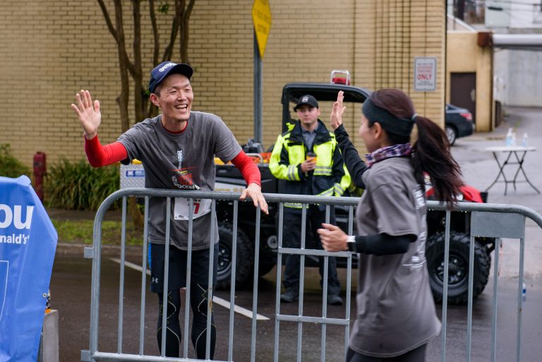 Male holds up his hand to high five a female runner as she cross the finish line