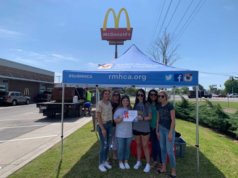 a group of women pose for a picture in front of McDonald's. A Recycling truck is off to the side