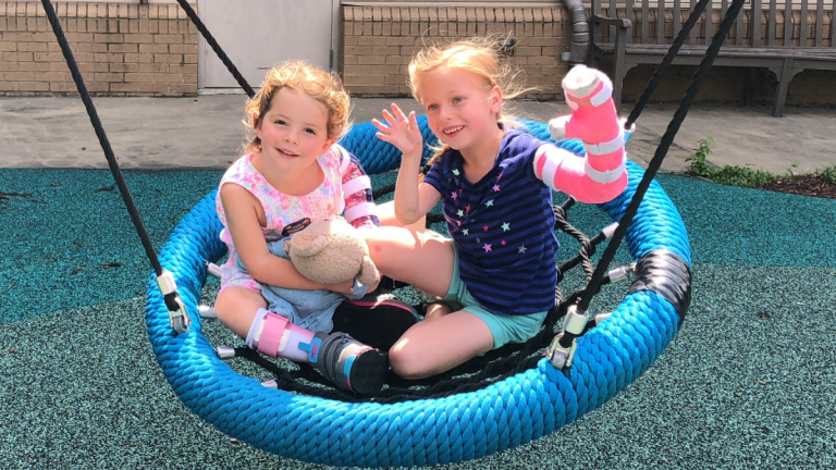 two young girls sit in a netted swing