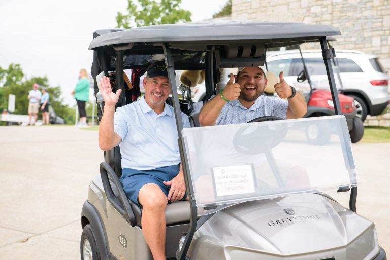 Two men wave from a golf cart
