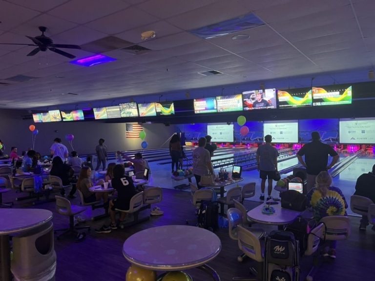 People in a darkened bowling alley bowling with glow in the dark balls.