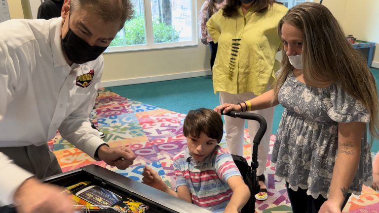 A mother watches while her son, who uses a wheelchair, plays pinball