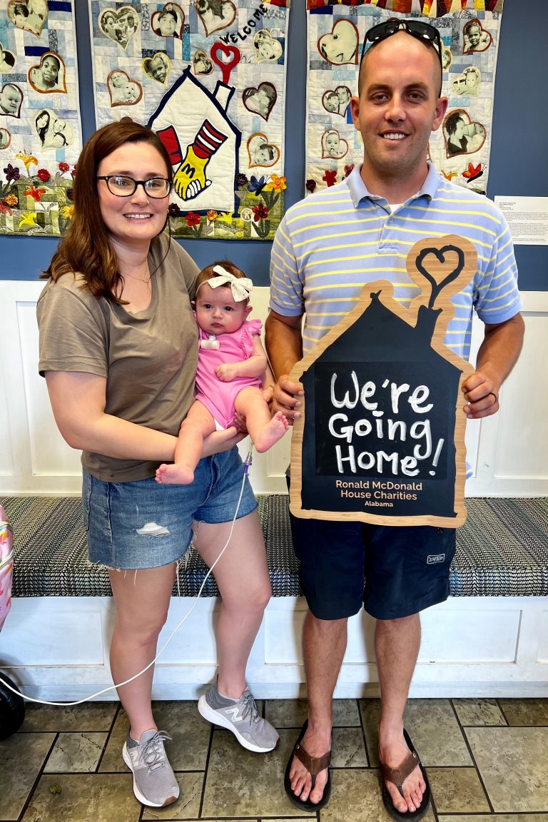 A family poses for a photo with a sign that says "We're going home!"