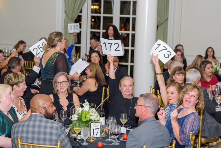 Women and men in evening finery smile during the bidding