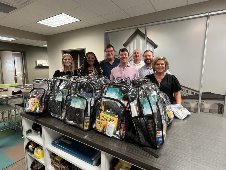 Seven adults proudly show off the backpacks and school supplies donated to RMHC of Alabama