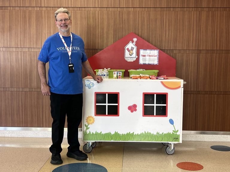 Happy wheels cart volunteer posed next to RMHC Happy wheels cart.