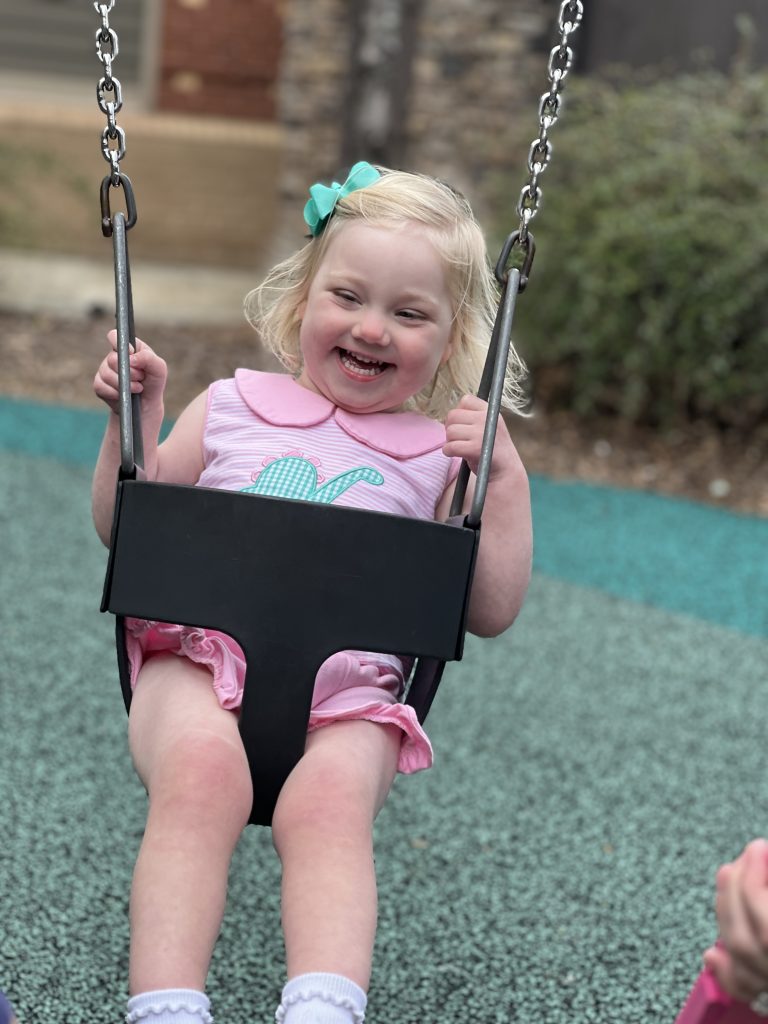 Little girl in pink dress swinging on the playground. 